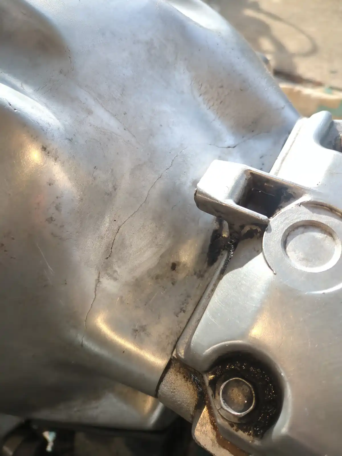 A close-up photo shows a cracked metal engine part, likely an engine block or cover, with visible dirt and oil stains. The…