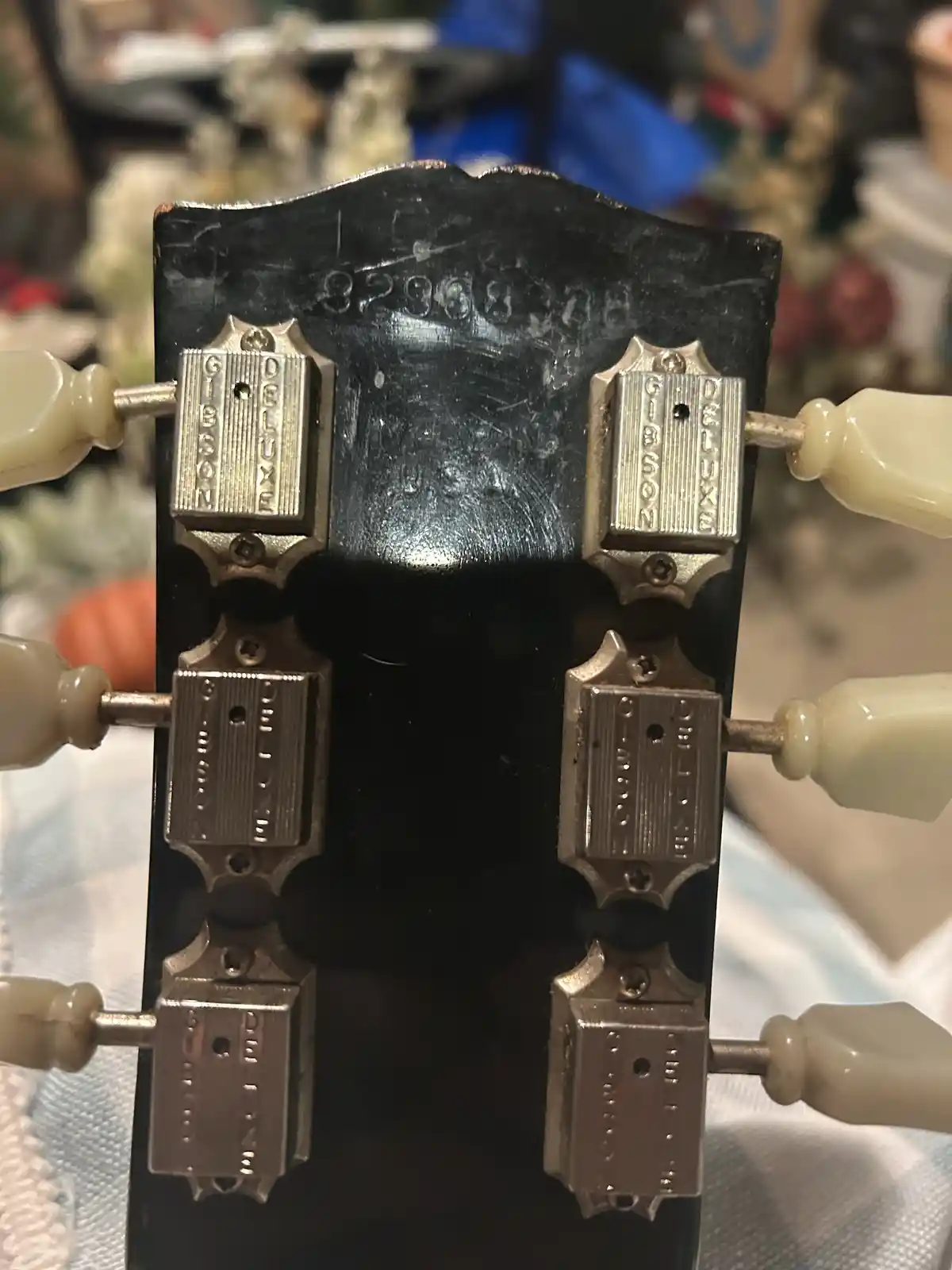A close-up of a vintage Gibson guitar headstock with six cream-colored tuning pegs and engraved metal plates that read…