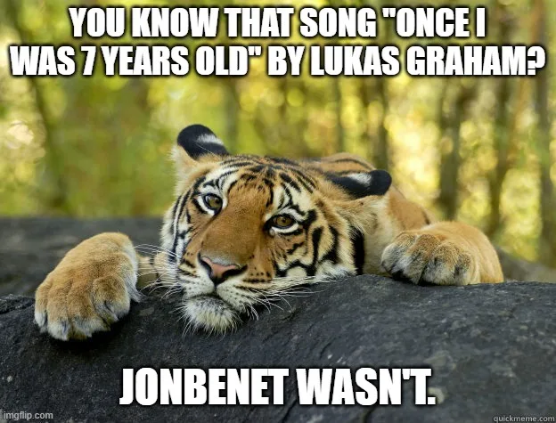 A young tiger cub lies on a dark log in a forest, looking directly at the camera with a calm, slightly bored expression…