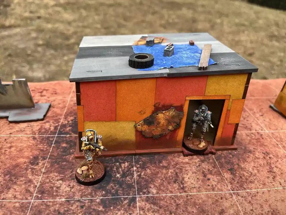 A miniature wargaming scene shows two heavily armored figures with red cross insignia on their gear, one standing outside a…