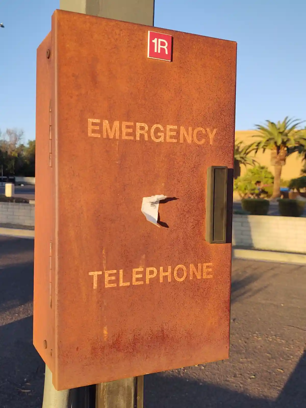 A rusty, outdoor emergency telephone box with 'EMERGENCY' and 'TELEPHONE' stenciled on its surface, featuring a small, torn…