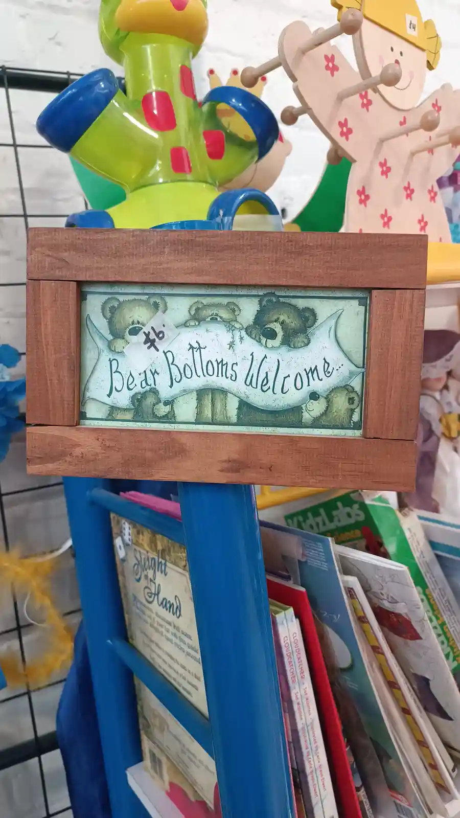 A wooden-framed sign in a children's store displays an illustration of cartoon bears holding a banner that reads 'Bear…