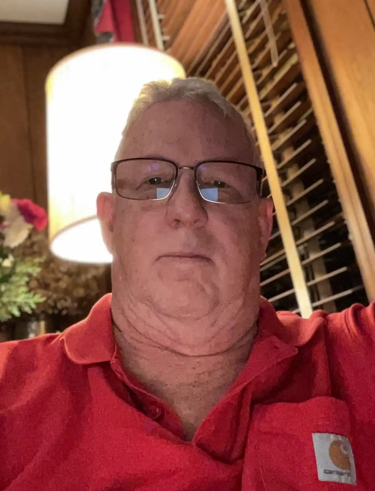 A close-up selfie of a middle-aged man with glasses and a red Carhartt polo shirt, looking directly at the camera with a…