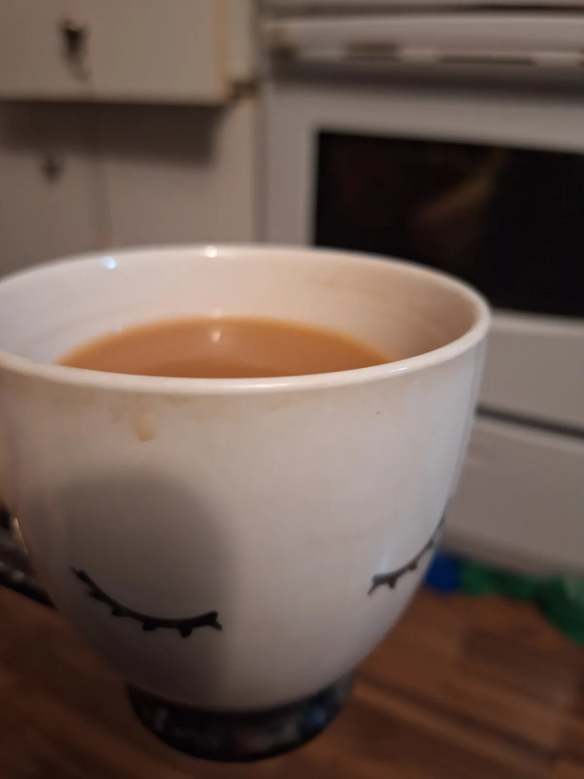 A close-up photo shows a white ceramic mug with a simple black line drawing of closed eyes, suggesting a sleepy or relaxed…