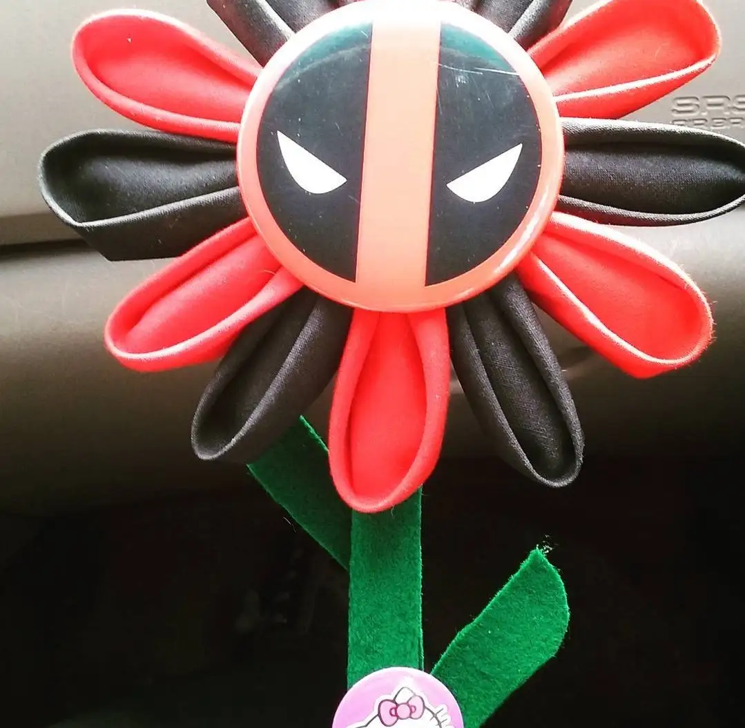 A handmade flower crafted from red and black fabric petals with a circular Deadpool mask at its center, attached to a green…