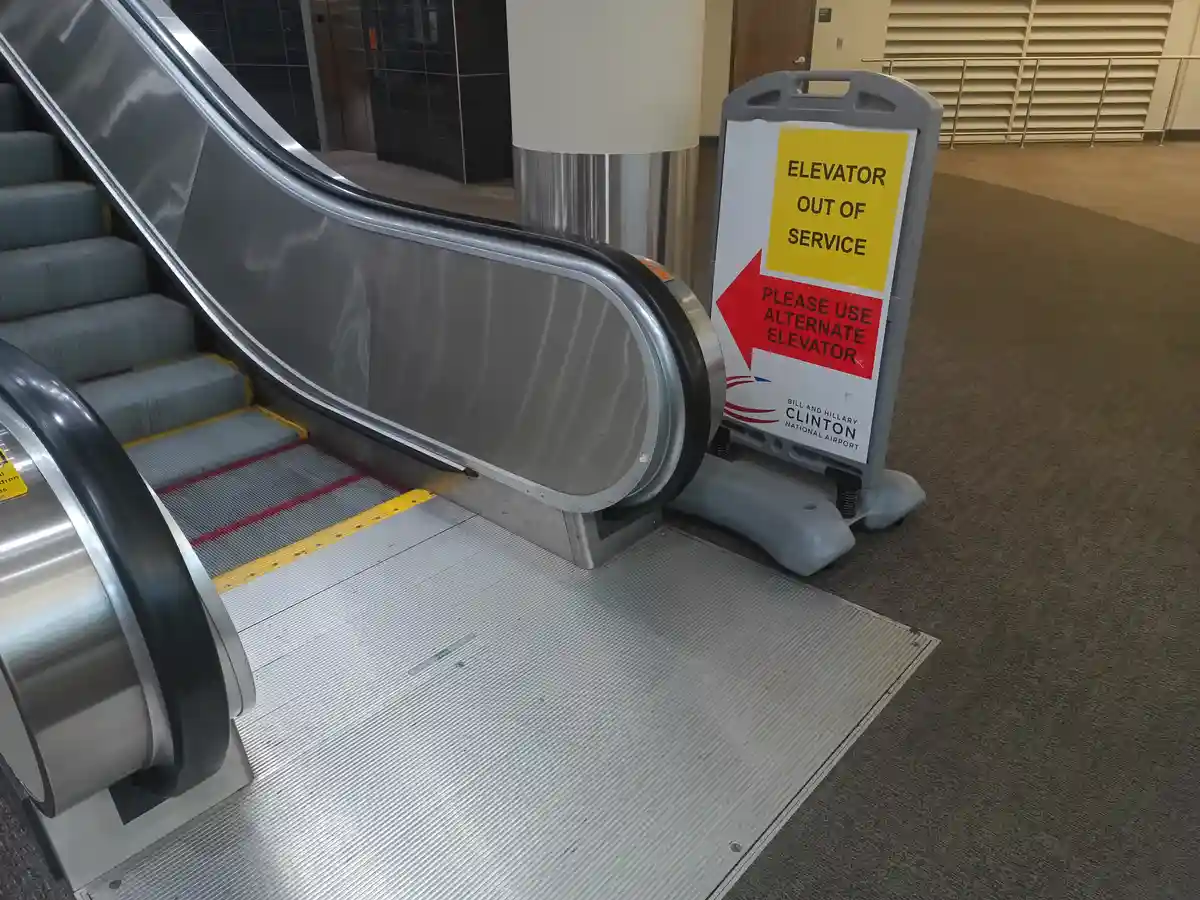 A photo shows a stationary escalator with a sign next to it that reads 'ELEVATOR OUT OF SERVICE PLEASE USE ALTERNATE…