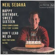 An album cover for Neil Sedaka featuring a smiling man in a red sweater holding a birthday cake with lit candles. The text…