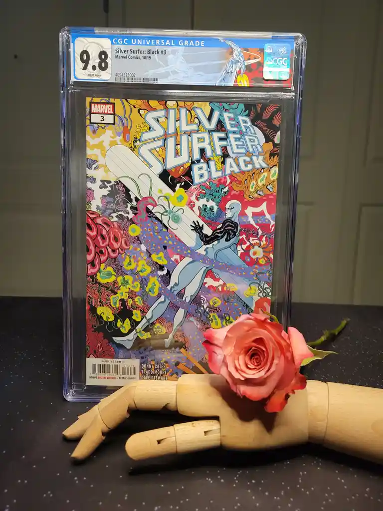 A CGC-graded Silver Surfer: Black #3 comic book (grade 9.8) is displayed upright in a clear protective case, with a wooden…