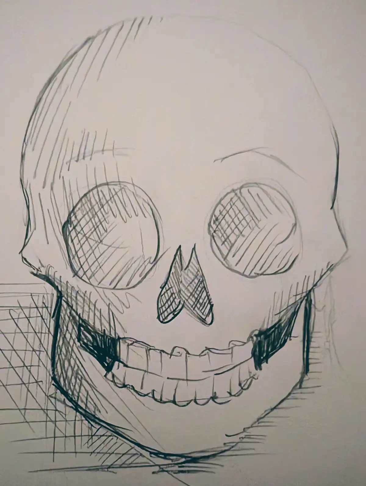 A hand-drawn sketch of a skull with large eye sockets, a triangular nose, and a wide, toothy grin. The skull is shaded with…