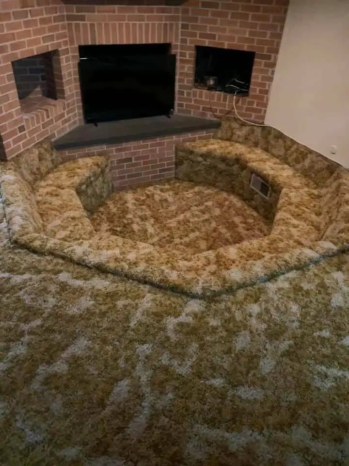 A room features a built-in, circular, low-profile seating area upholstered in shaggy, patterned fabric that resembles a…
