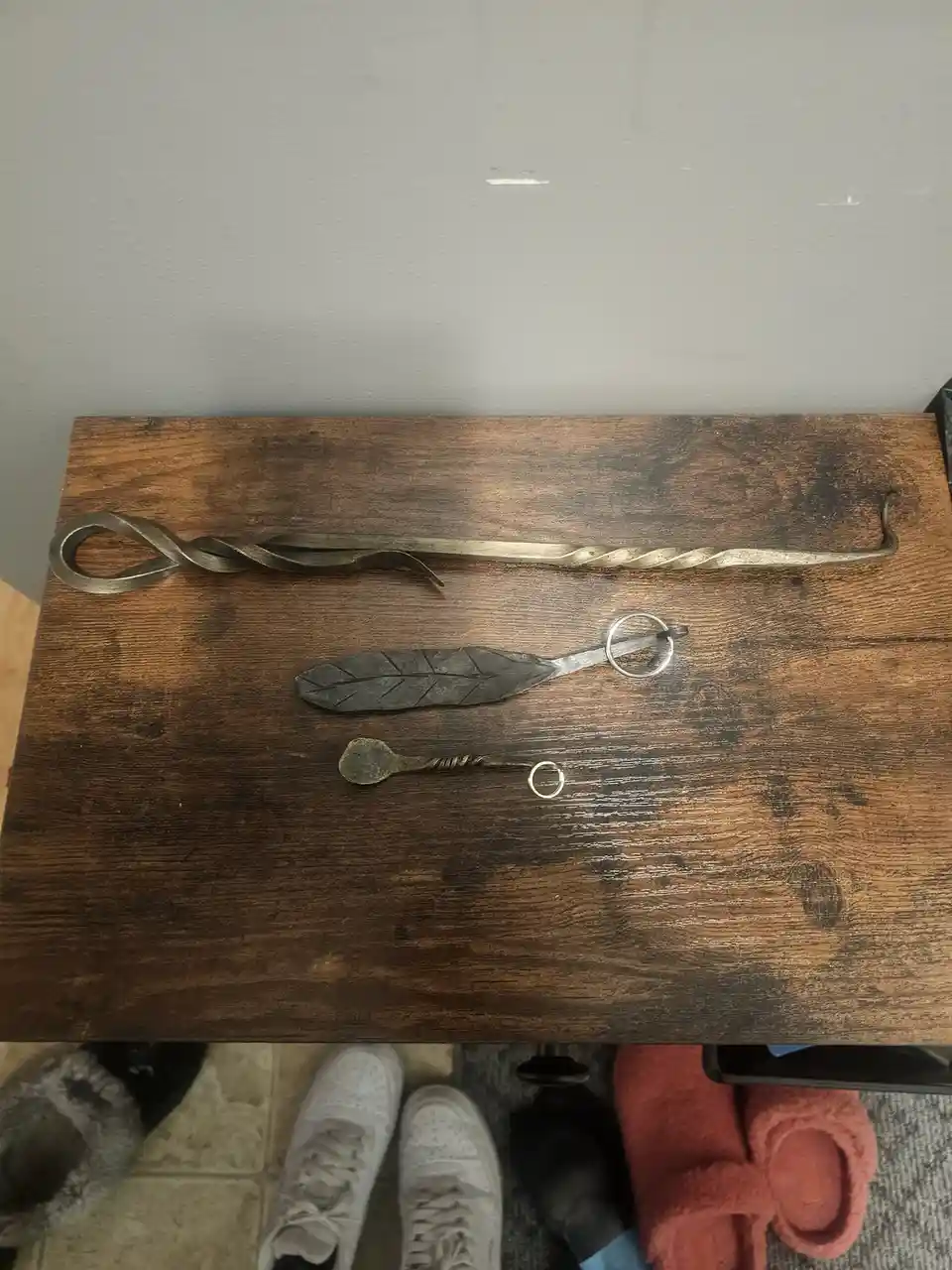Three decorative metal keychains shaped like a twisted staff, a feather, and a spoon lie on a dark wooden table. Below, a…