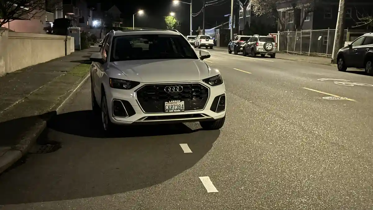A white Audi Q5 SUV is parked on a residential street at night, its front grille and headlights illuminated. The Washington…