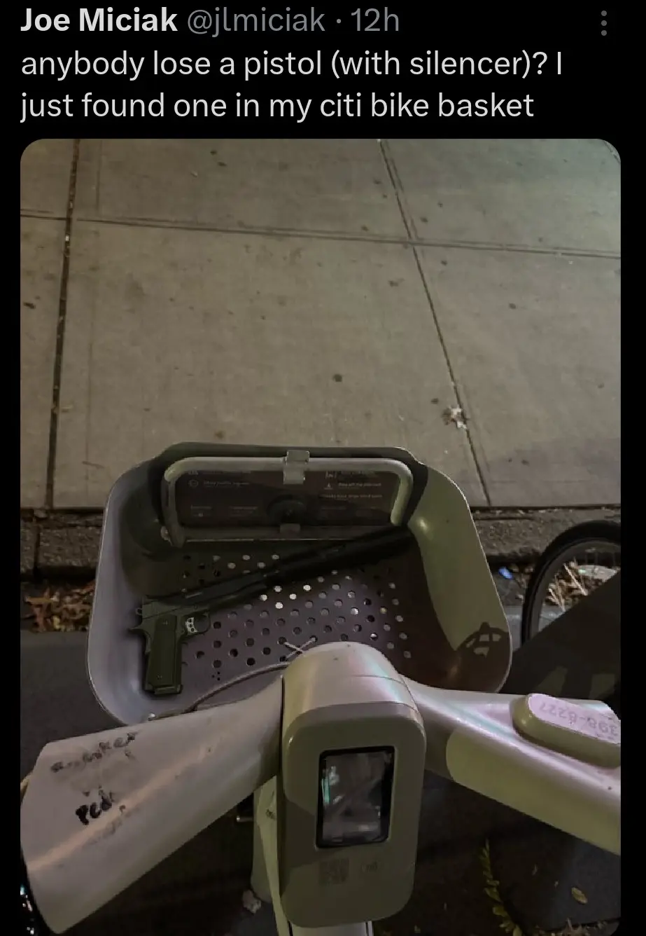 A photo shows a green pistol with a silencer resting inside the perforated metal basket of a Citi Bike, which is parked on a…