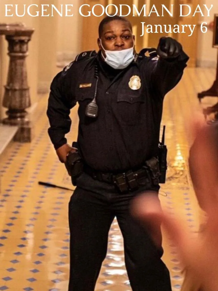 A Black police officer in uniform stands in a hallway with a patterned floor, wearing a face mask and pointing forward with…