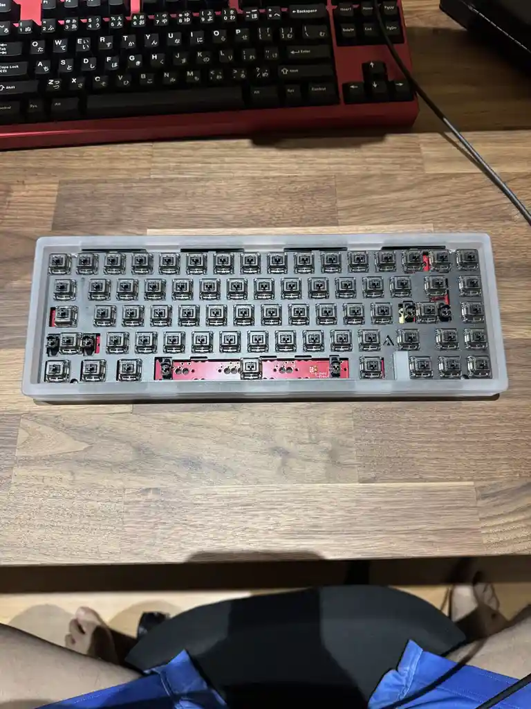 A top-down photo shows a disassembled mechanical keyboard with its keycaps removed, revealing the red circuit board and…