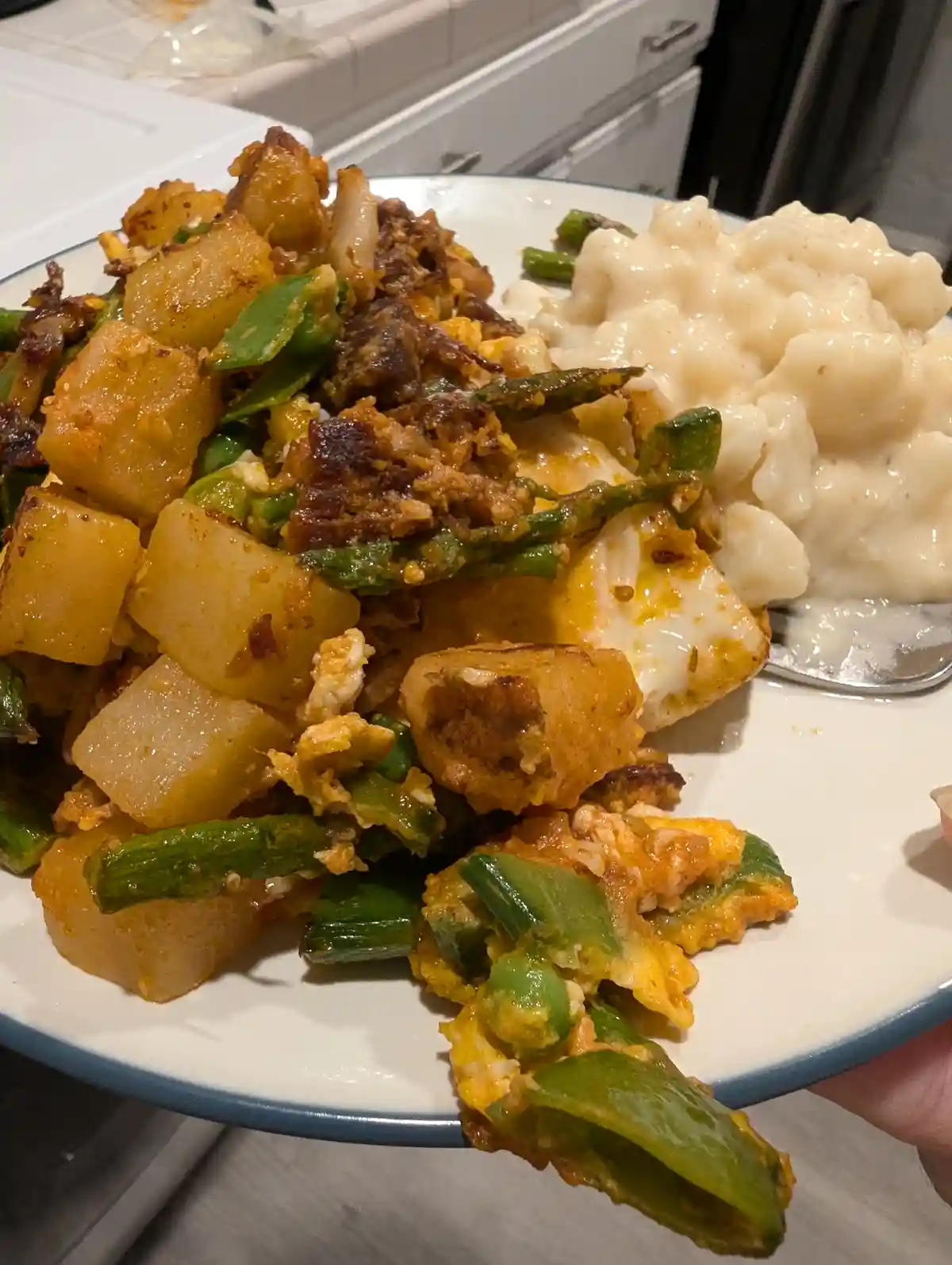 A close-up photo shows a plate of home-cooked food, featuring a mix of diced potatoes, green beans, scrambled eggs, and what…