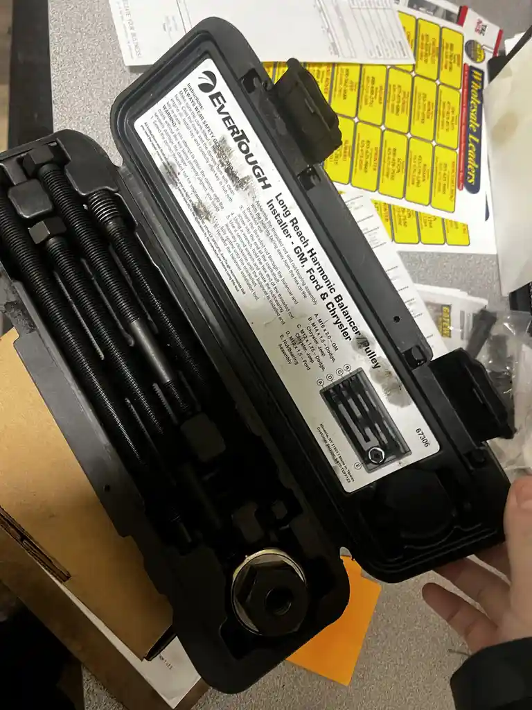 A hand holds open a black plastic case containing a specialized automotive tool kit labeled 'EverTough Long Reach Harmonic…