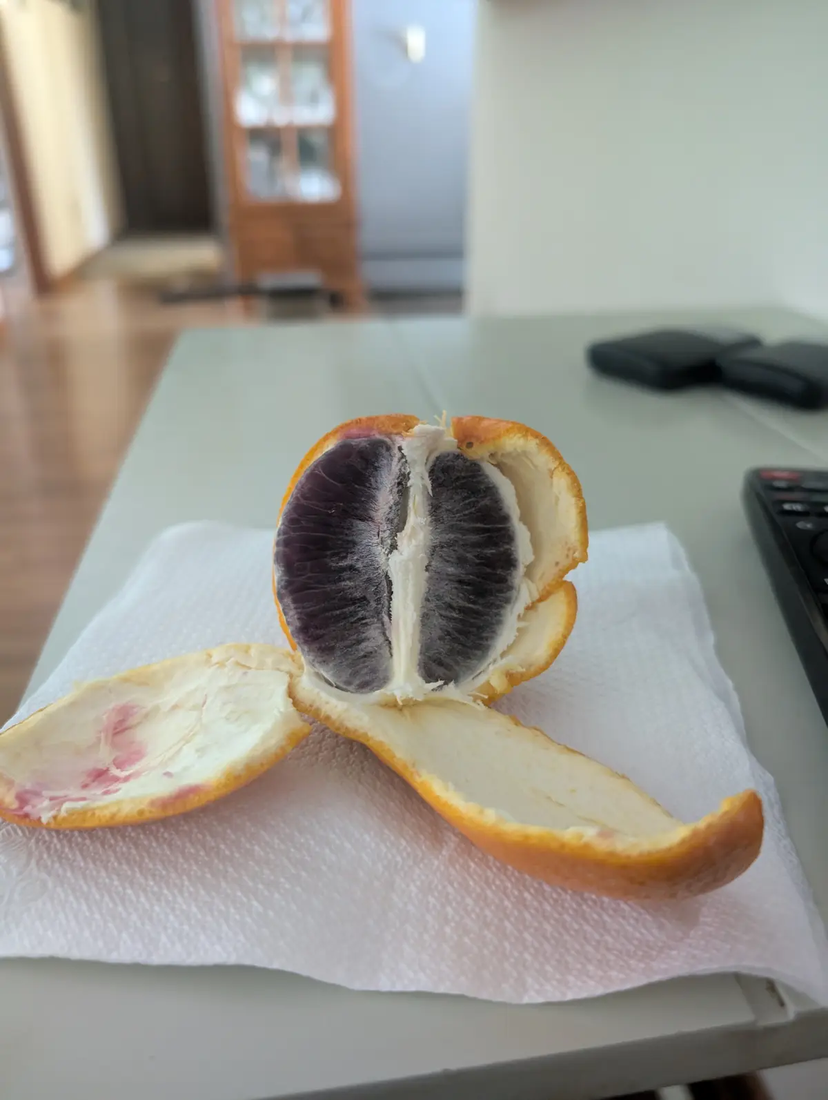 A halved citrus fruit, likely a blood orange, sits on a paper towel on a kitchen counter, its flesh appearing dark purple…