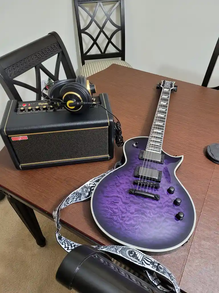 A purple electric guitar with a swirling finish and a black-and-white patterned strap rests on a wooden dining table next to…