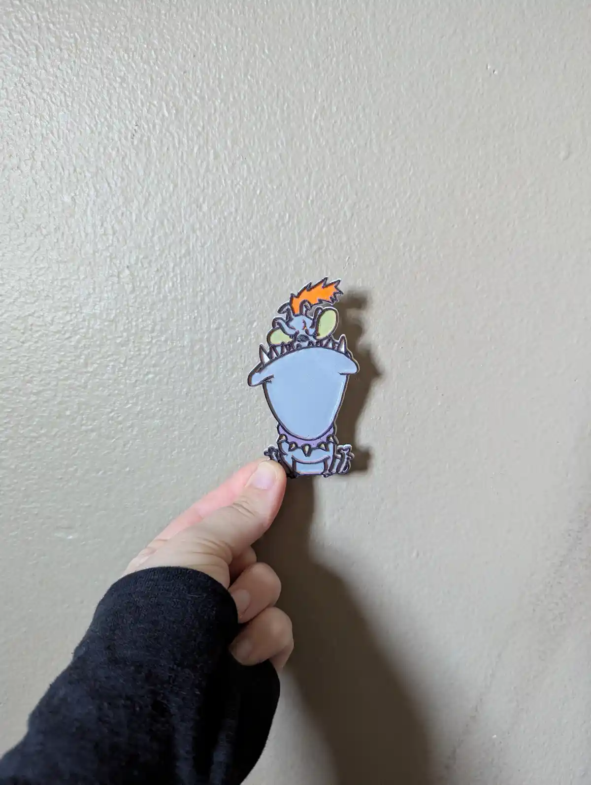 A hand holds up a small enamel pin featuring the character 'Squidward' from SpongeBob SquarePants, depicted with his…