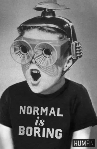 A black-and-white photo of a young boy wearing a futuristic-looking helmet with large fan-like goggles and a small dome on…