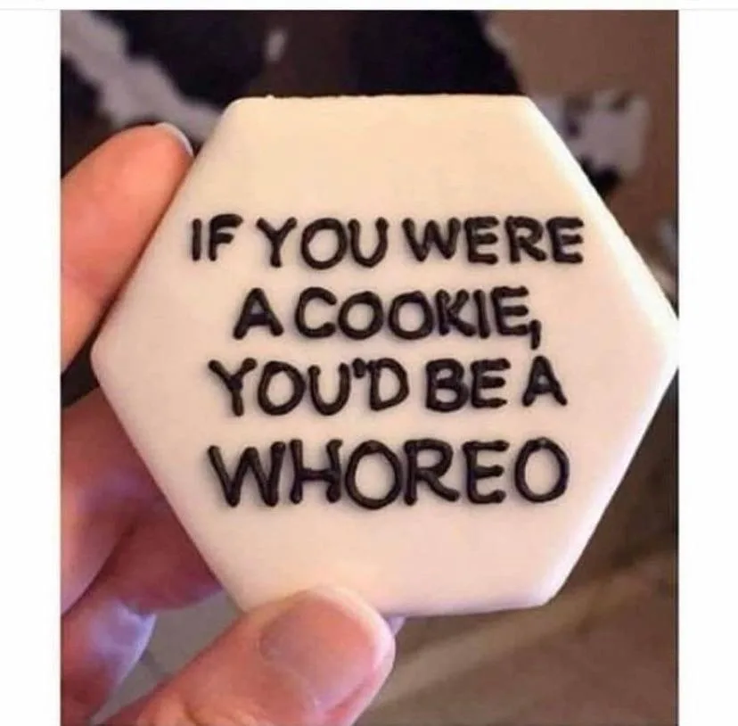 A hand holds a hexagonal, white-frosted cookie with black icing text that reads 'IF YOU WERE A COOKIE, YOU'D BE A WHOREO'…