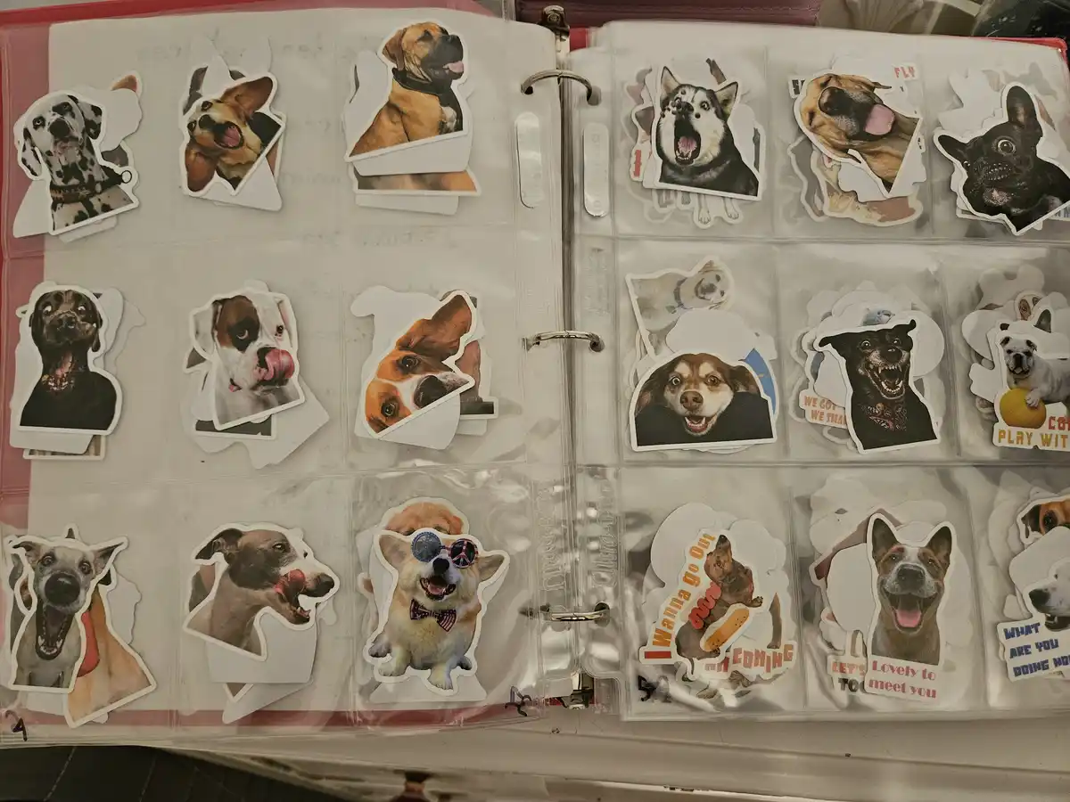 An open binder filled with clear plastic sleeves containing numerous dog stickers, each showing a different breed or…