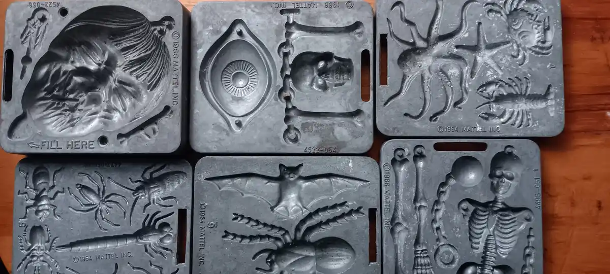 Six vintage 1960s Mattel metal molds for Halloween candy, showing spooky designs like a witch, skull and bones, sea…