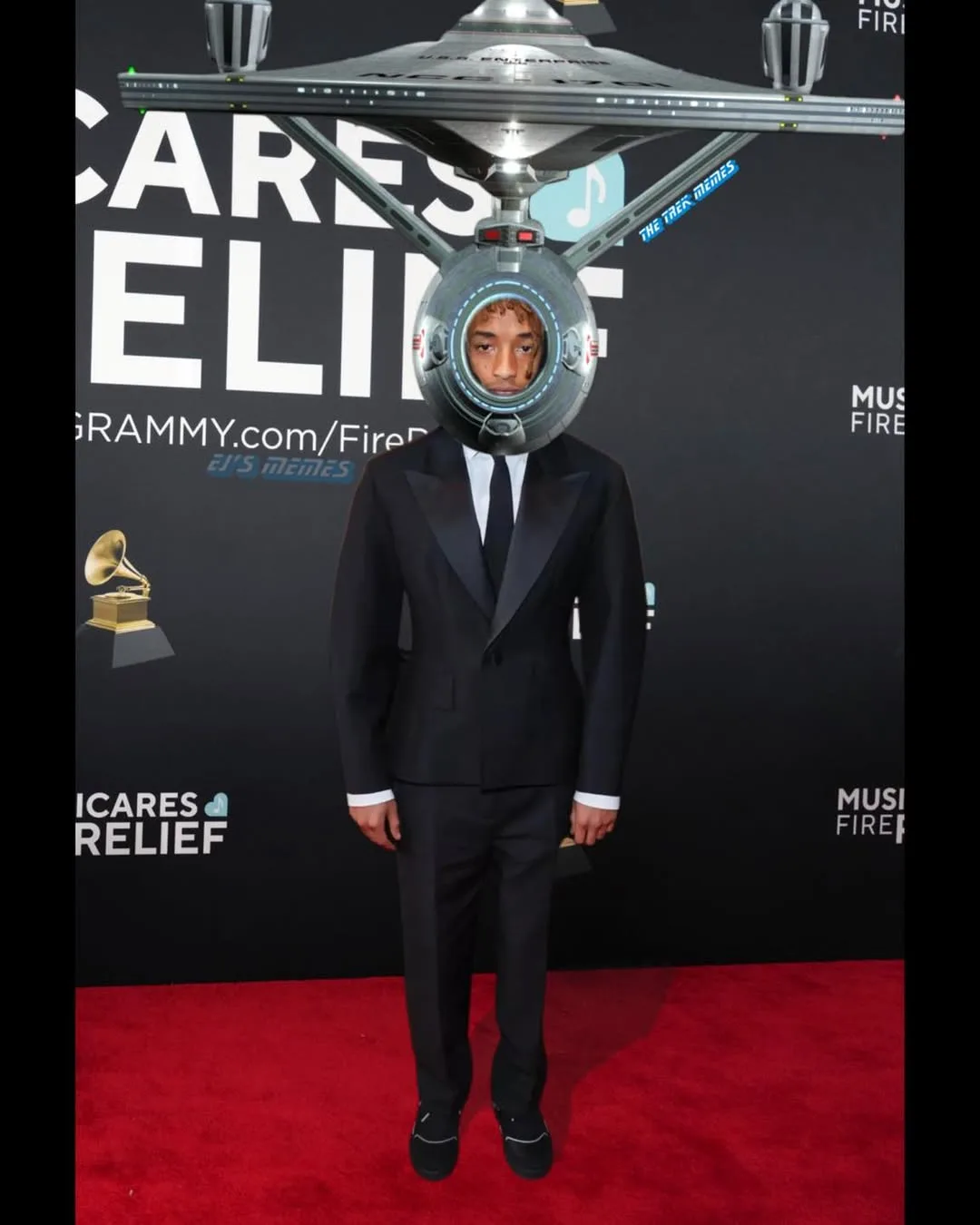A man in a black tuxedo stands on a red carpet at a GRAMMYs event, with a Star Trek Enterprise spaceship digitally edited to…