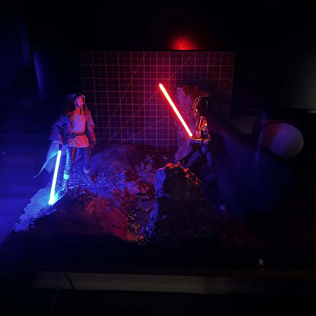 Two Star Wars action figures, one as a Jedi with a blue lightsaber and one as Darth Vader with a red lightsaber, are posed…