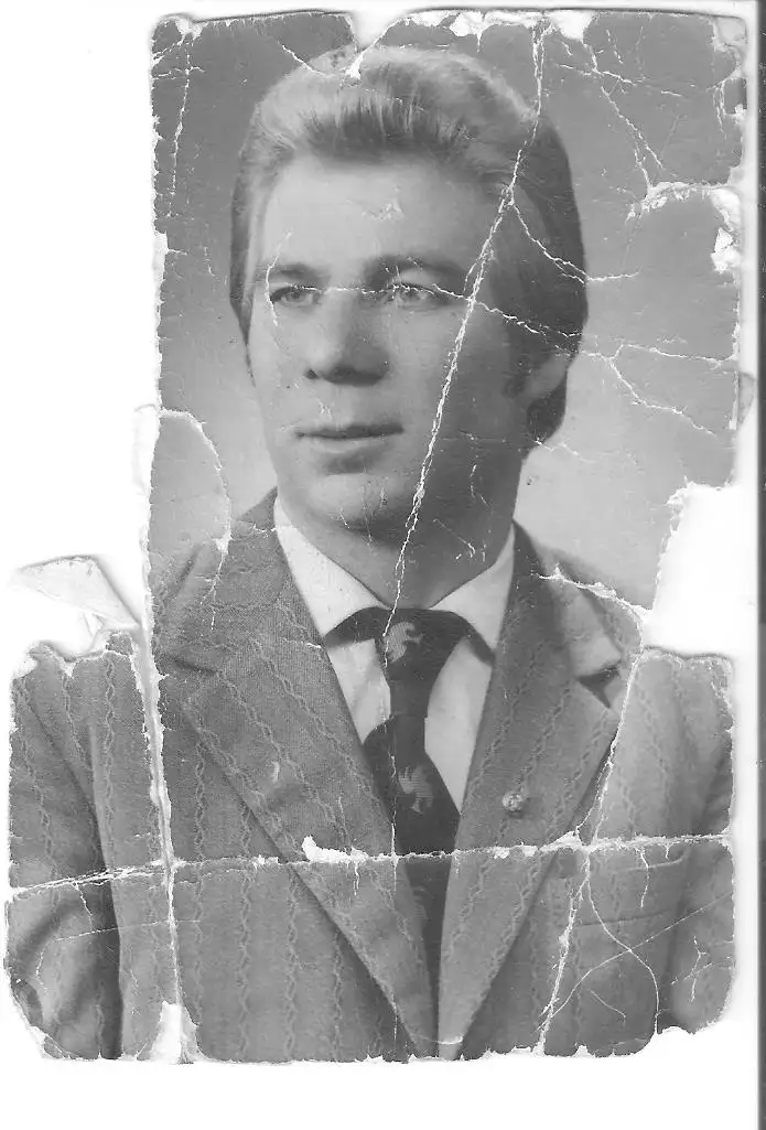 A heavily cracked and torn black-and-white vintage portrait of a man in a suit and tie, looking directly at the camera. The…