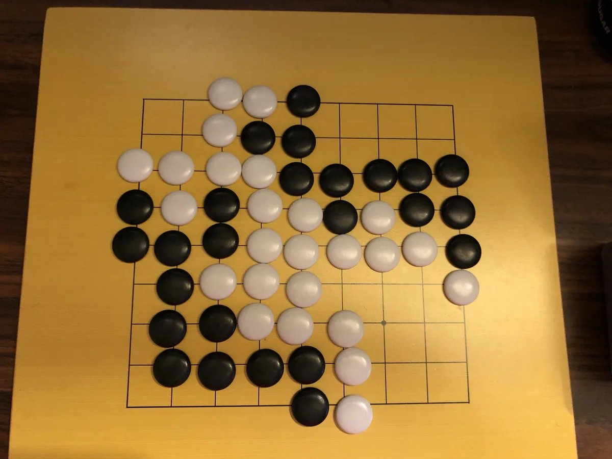An overhead photo of a Go board with black and white stones arranged in a pattern that visually resembles a person's face…