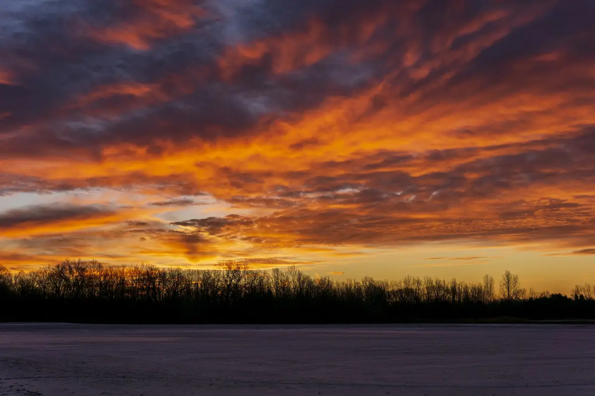 A dramatic sunset with fiery orange and purple clouds over a frozen field and silhouetted trees. The overlaid text reads…