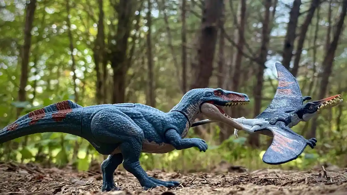 Two plastic dinosaur toys, a blue theropod and a blue pterosaur, are staged in a forest setting with the pterosaur appearing…