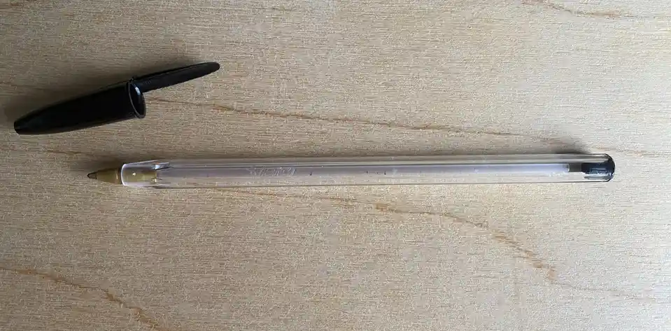 A clear BIC pen with its black cap lying separately on a light wood-grain surface, visually implying the pen is 'empty' or…