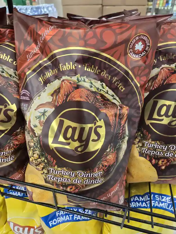 A close-up of a bag of Lay's potato chips featuring a festive design with a roasted turkey on mashed potatoes, labeled…