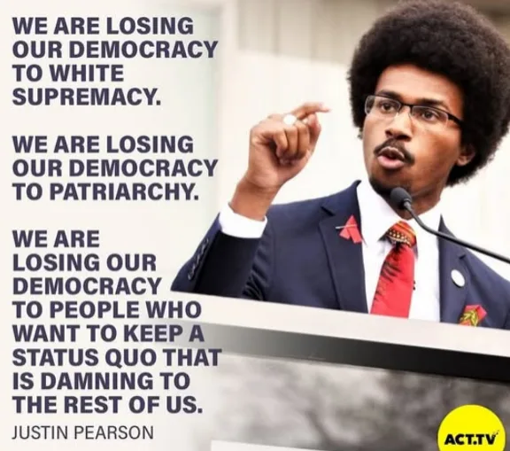 A man with an afro, glasses, and a suit stands at a podium speaking into a microphone. Overlaid text lists three statements…