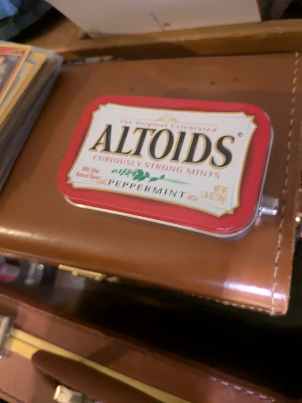 A red and white Altoids peppermint tin sits on a brown leather surface, with the brand's slogan 'Curiously Strong Mints'…