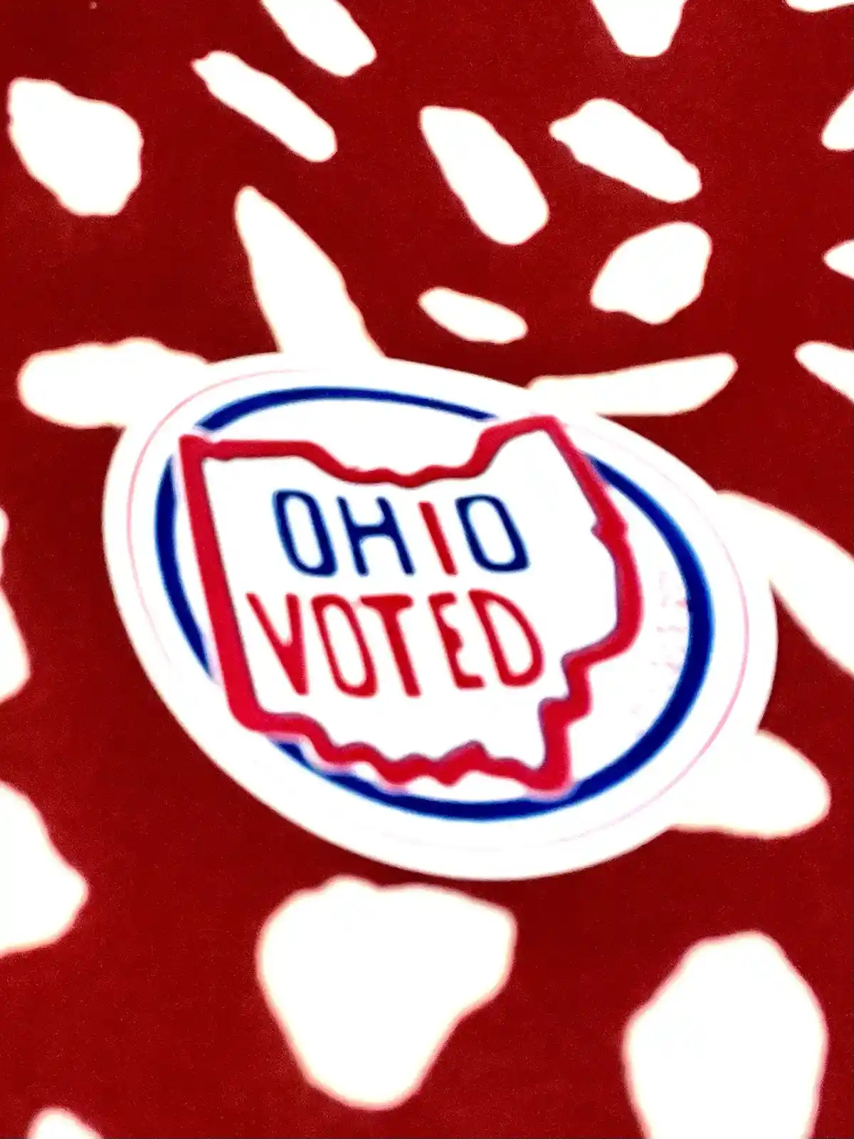 A close-up of a red and white sticker featuring the outline of the state of Ohio with the words 'OHIO VOTED' inside, set…