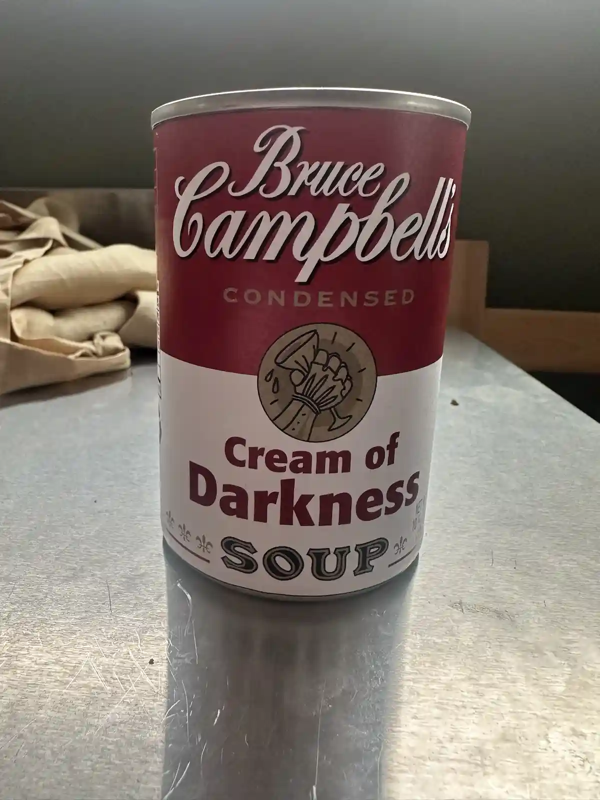 A can of soup sits on a metal surface, its label parodying Campbell's Soup branding but with 'Bruce Campbell's' at the top…