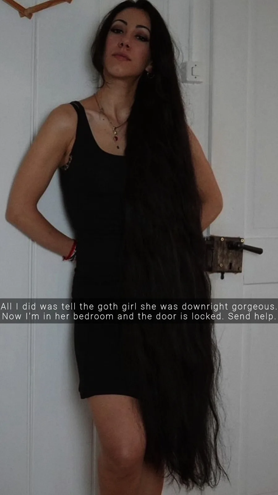 A woman with extremely long, dark hair stands in front of a white door, her hair draped over her body and partially…