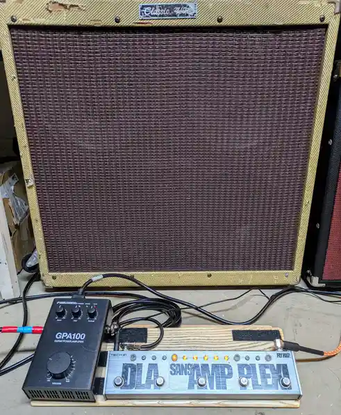 A large, vintage-style guitar amplifier with a worn tan tolex and brown grille cloth sits behind a small black PedalTech…
