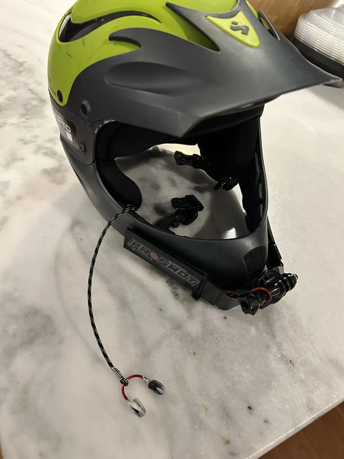 A lime green and black mountain bike helmet sits on a white marble surface with a GoPro camera mounted on its chin strap…