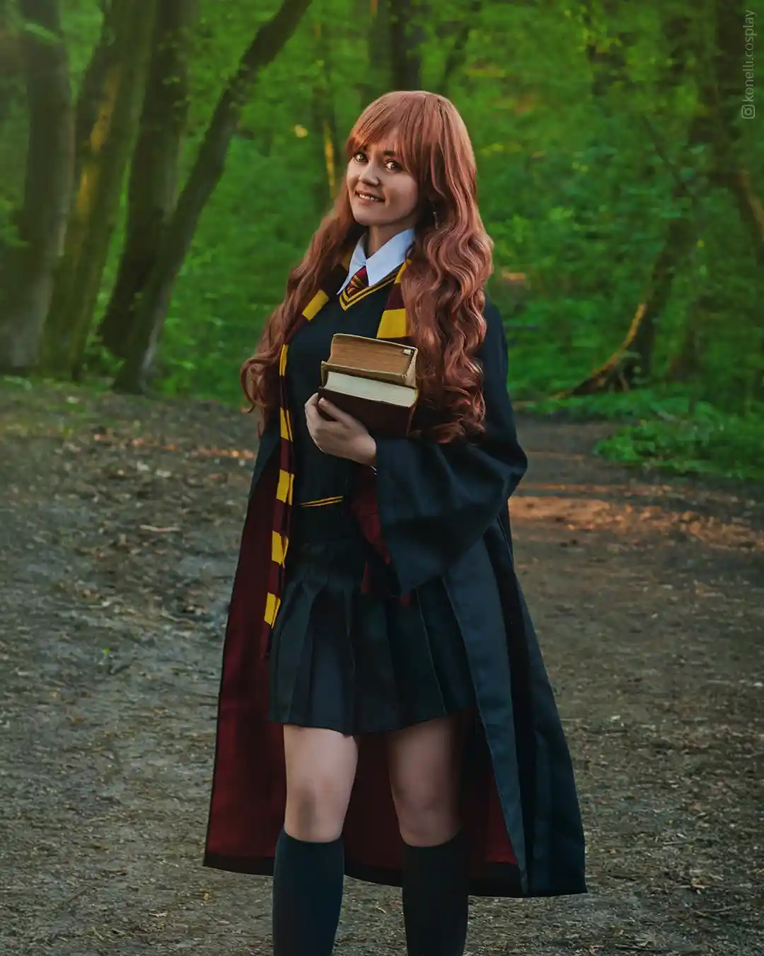 A person in a Harry Potter cosplay, dressed as a Gryffindor student with a maroon and gold scarf, holding books, stands on a…