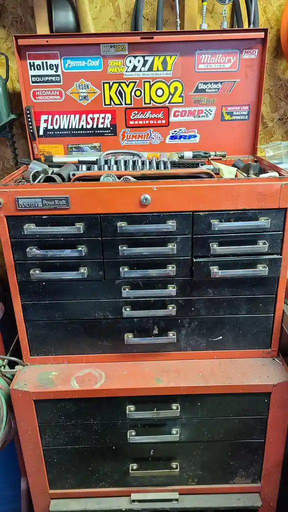 An orange Montgomery Ward Powr-Kraft tool chest with its lid open, revealing various tools inside and covered in numerous…