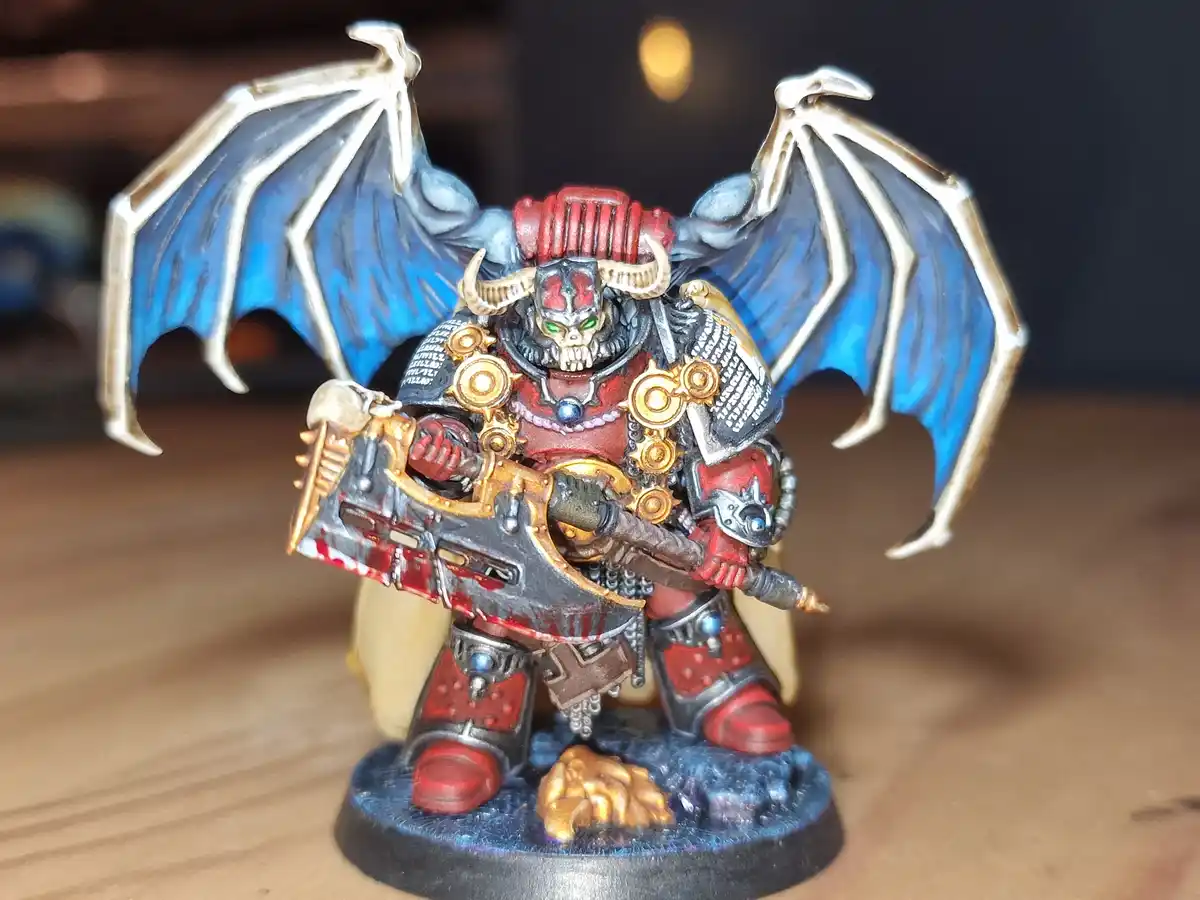 A heavily detailed, hand-painted miniature figurine of a demonic warrior with large blue bat-like wings, a skull helmet with…