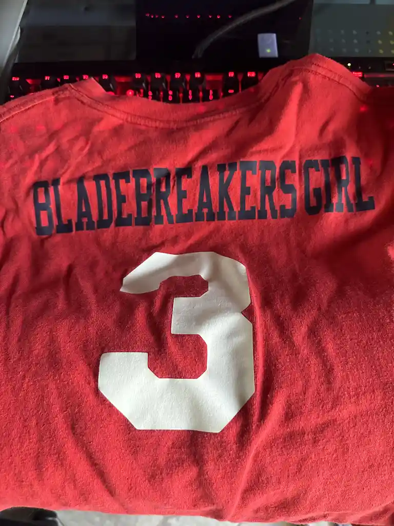 A red t-shirt with the text 'BLADEBREAKERS GIRL' in black block letters across the back and a large white number '3' below…