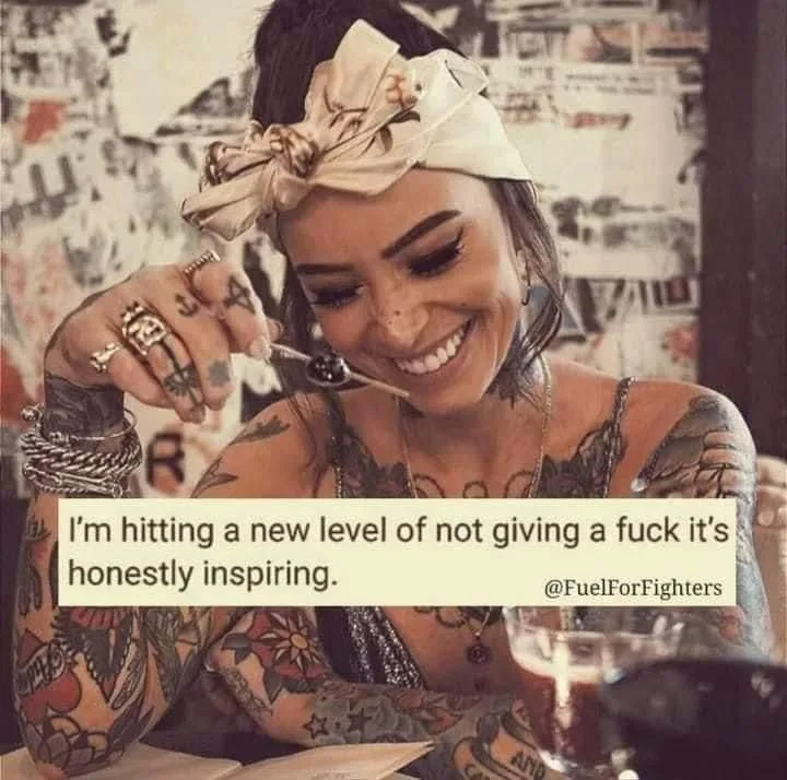 A smiling woman with tattoos on her arms and neck, wearing a large bow headband and multiple rings, holds a spoon to her…