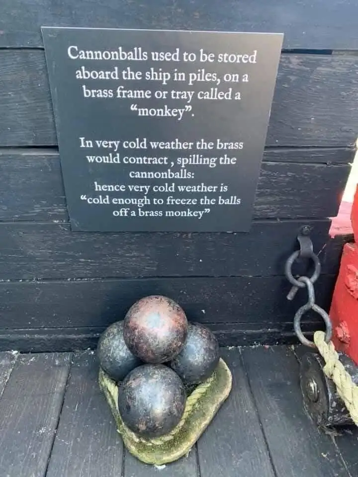 A black informational plaque mounted on dark wood explains the origin of the idiom 'cold enough to freeze the balls off a…
