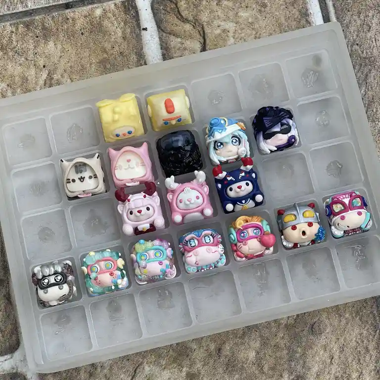 A transparent plastic ice cube tray holds 16 small, colorful, custom-made figurines resembling cartoon characters and anime…